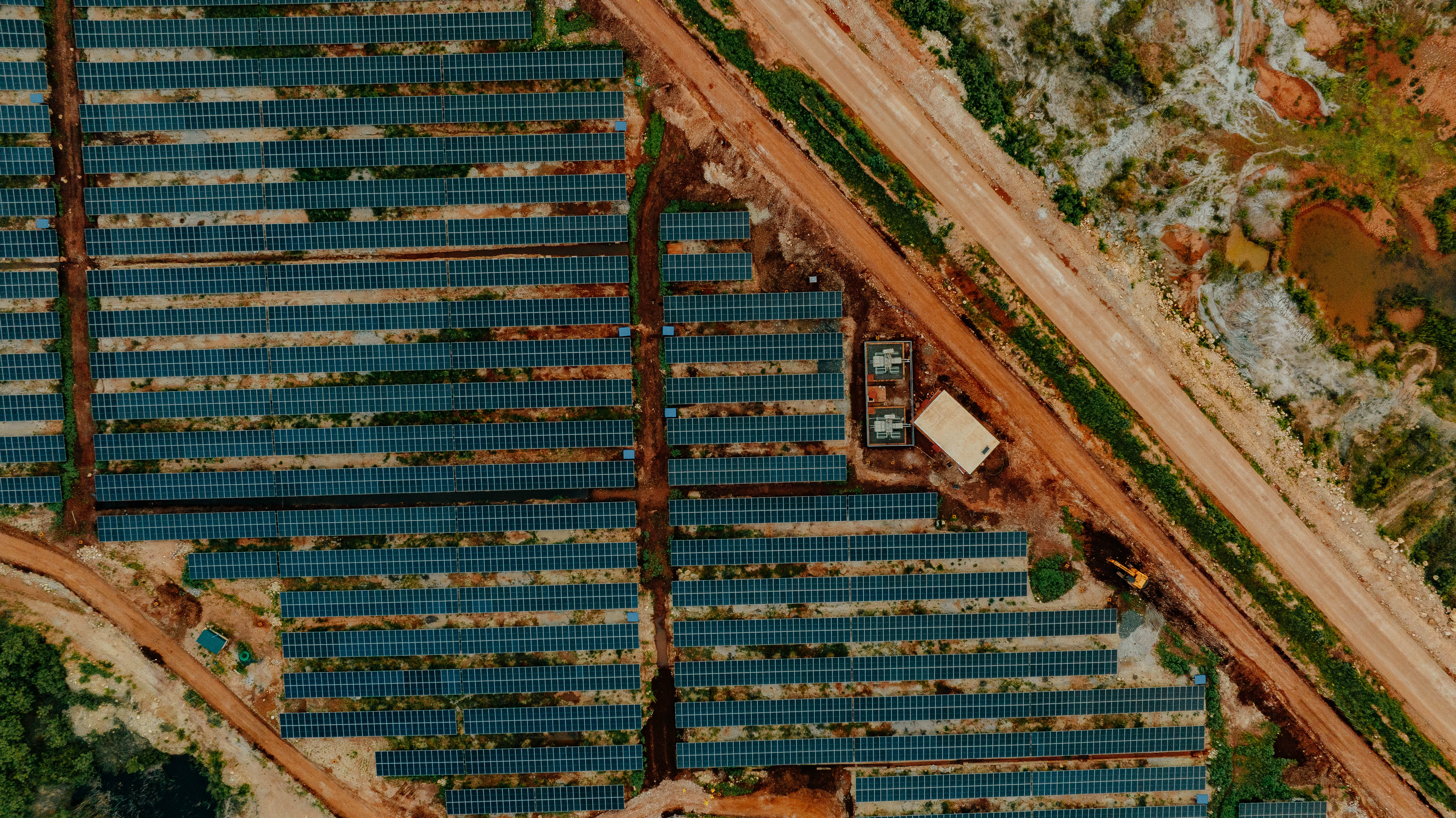 Aerial view of a solar panel installation at an industrial site surrounded by construction and natural terrain.