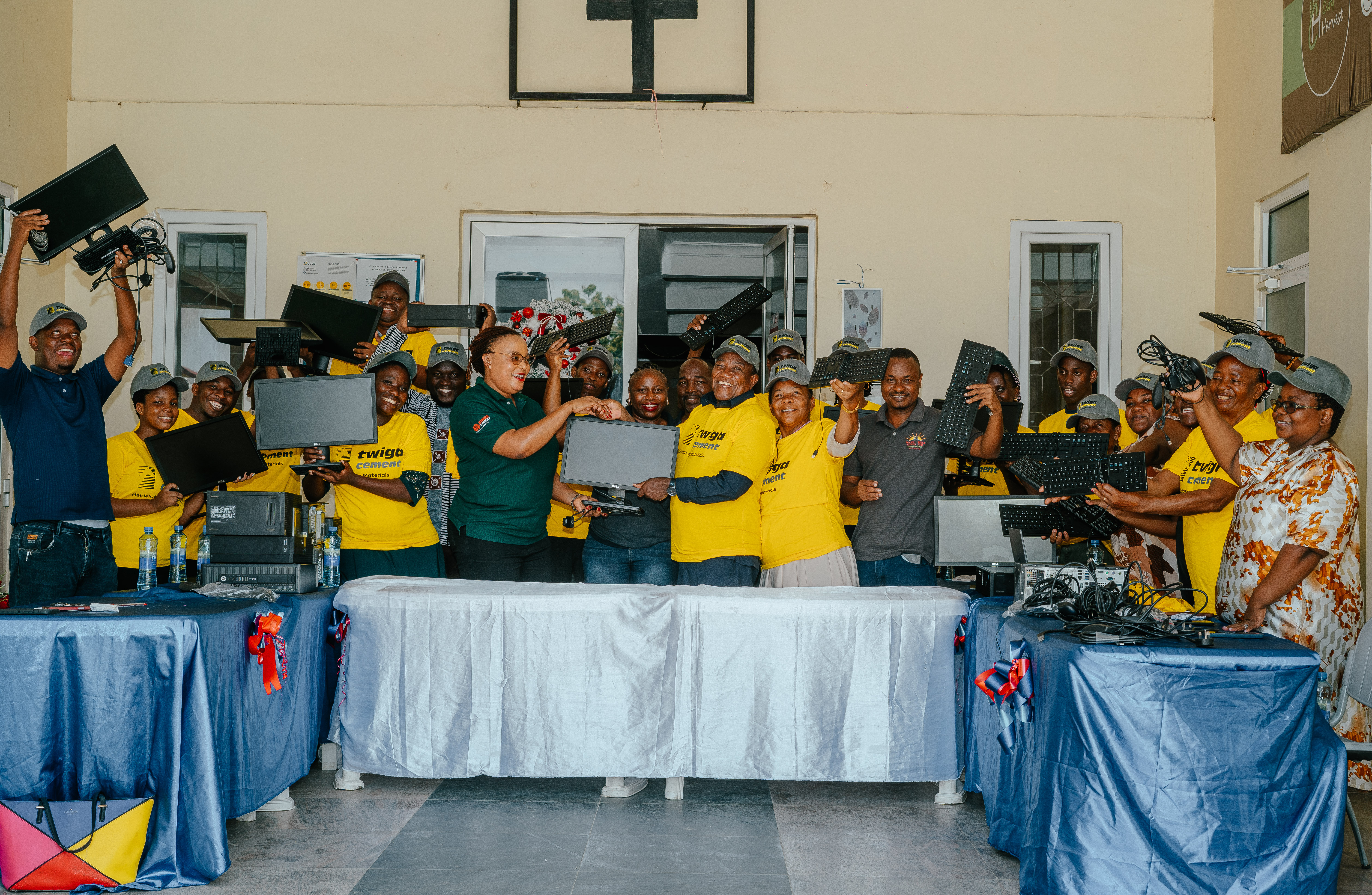 A group of people, some wearing yellow shirts, celebrating while holding up laptops in an outdoor setting.