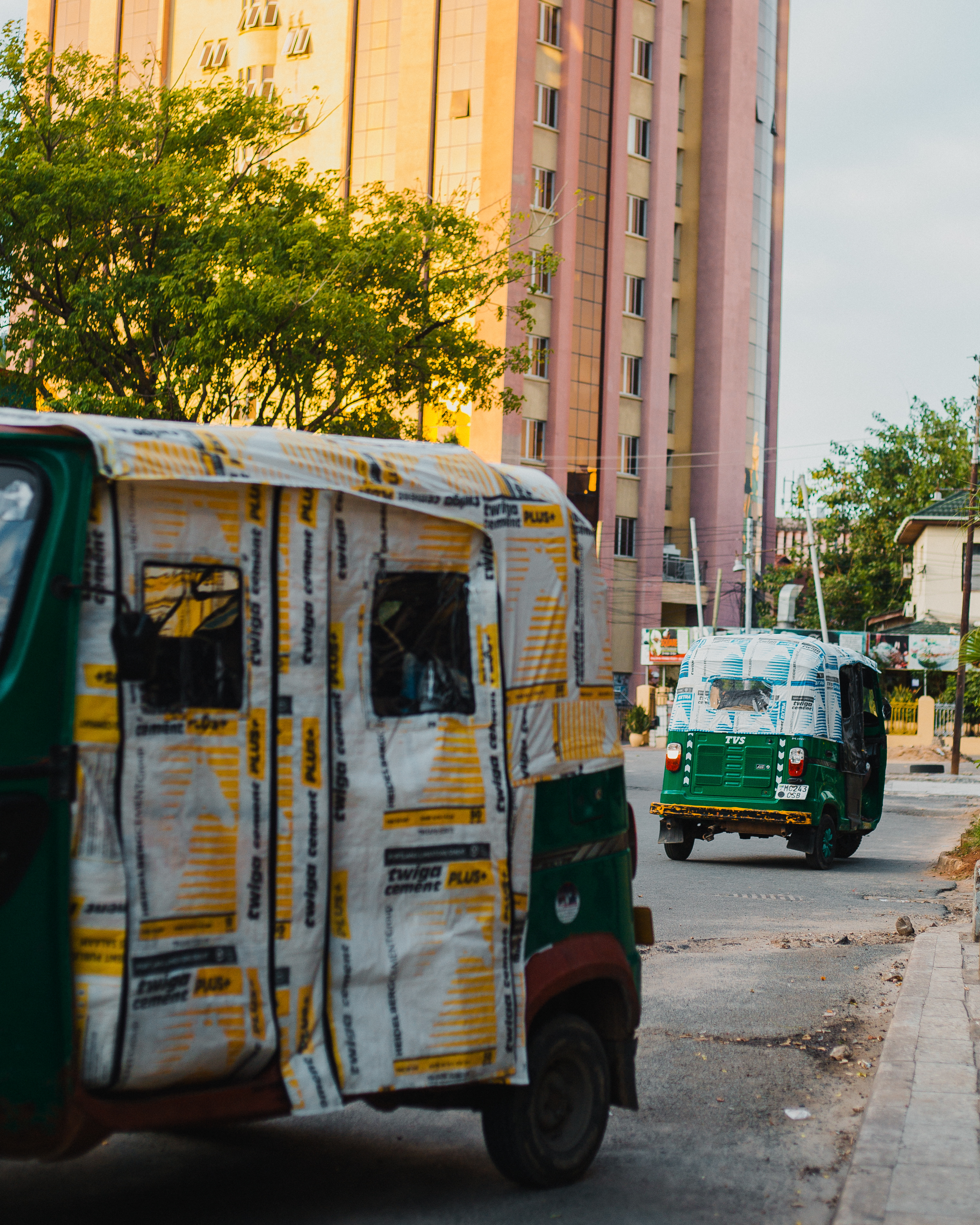 Motorized rickshaws covered with Heidelberg Materials-branded packaging drive through an urban area.