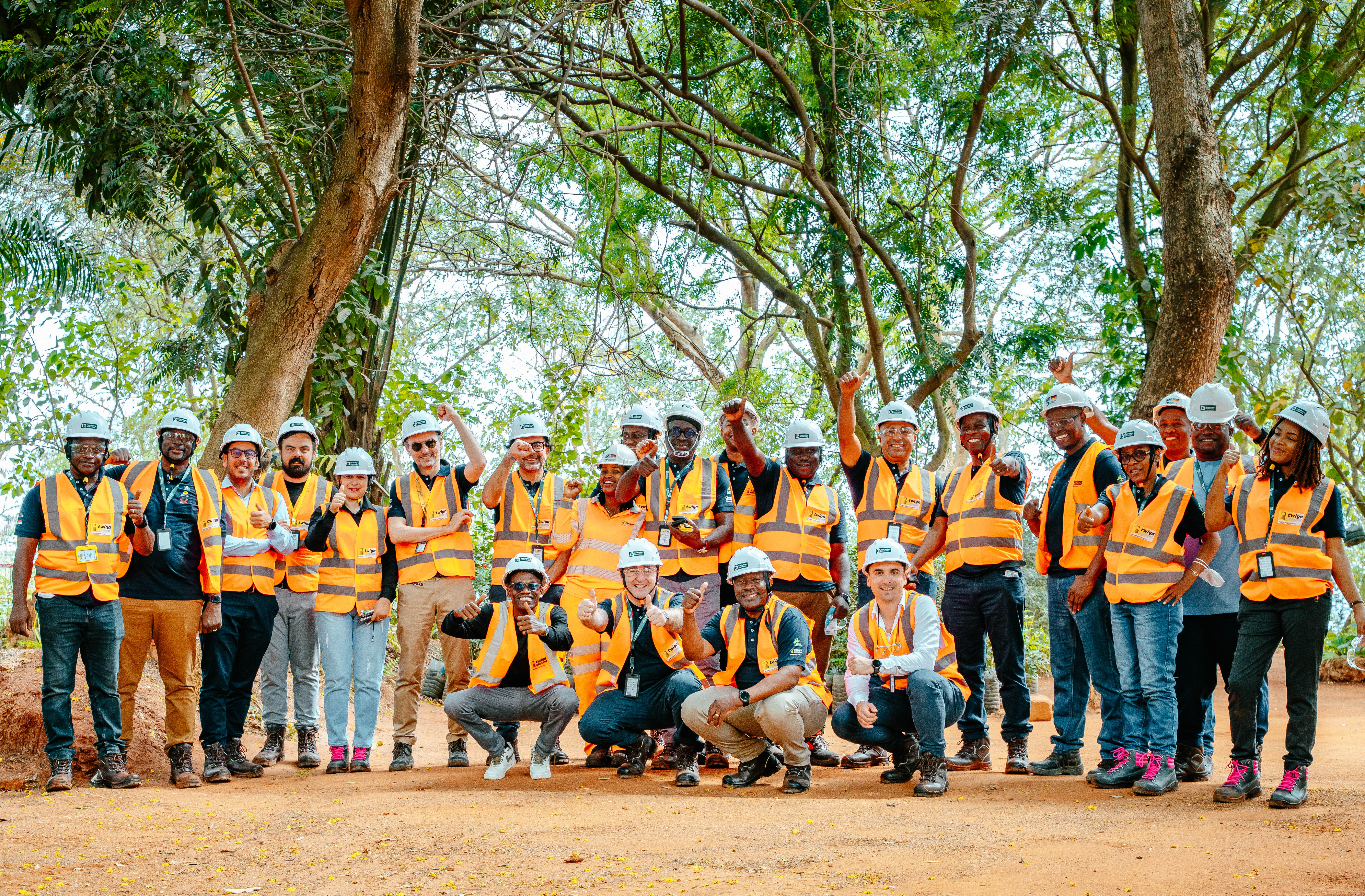 A group of workers in safety vests and helmets poses outdoors at a construction or industrial site.