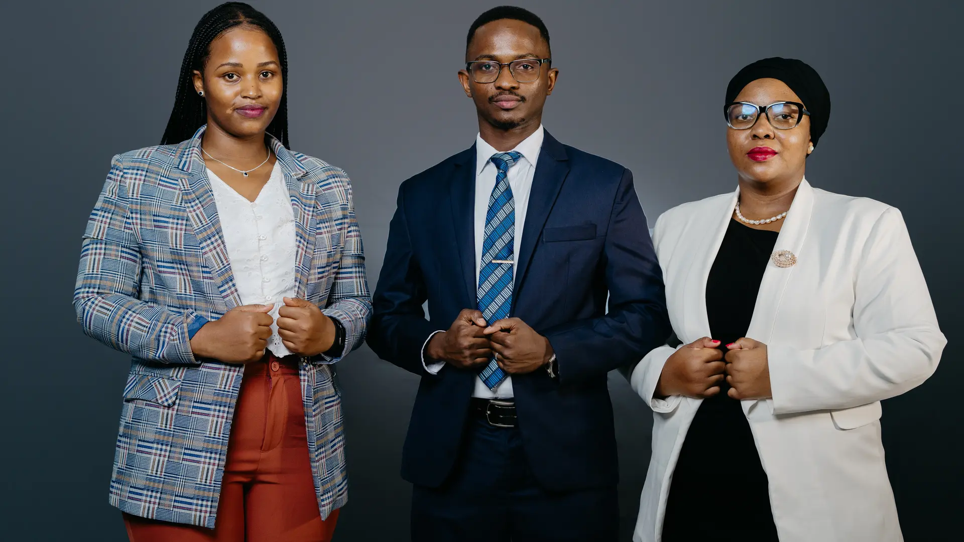 Three professionally dressed individuals standing confidently against a plain background.