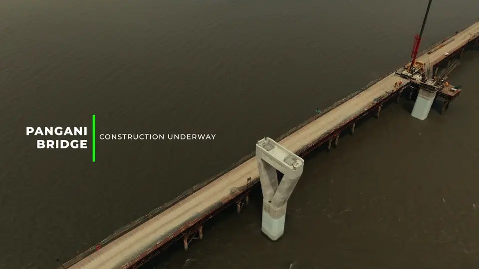 A partially constructed bridge spans over a wide river, with a crane positioned on the structure.